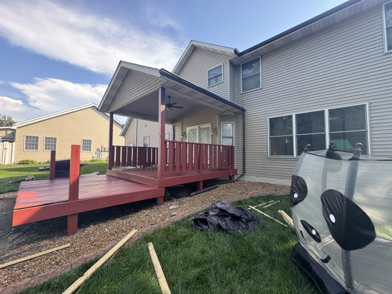 Wraparound deck finished in rich red solid stain with matching railings and spindles, hand-applied by TD Surface Stain and Seal