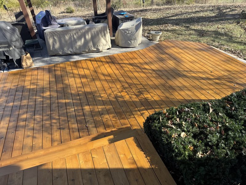 Cedar-natural stained deck near a tree with landscaping visible, hand-applied by TD Surface Stain and Seal